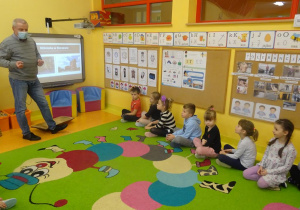 Pan Maciej Grzeszczak przedstawia dzieciom siedzącym przed tablicą interaktywną prezentację dotyczącą dawnych zamierających zawodów.